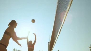 Slow Motion, Sun Flare, Close Up, Low Angle: Neşeli Kafkasyalı kız güneşli bir günde plaj voleybolunda bir puan aldı. Atletik kadınlar ve erkekler yaz tatillerinde voleybol oynuyorlar..
