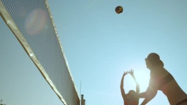 SLOW MOTION, CLOSE UP, LENS FLARE, LOW ANGLE: Athletic young Caucasian women in bikinis playing beach volleyball in the bright summer sun. Fit girls having fun playing volleyball in their bikinis.