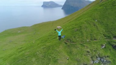 Uçurumun kenarında kollarını açıp nefes kesici okyanusa bakan neşeli bir kadın vardı. Dişi turist, Faroe Adaları 'ndaki dik otlak bir dağa çıktıktan sonra mutlu..