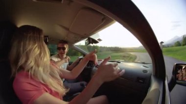 Slow Motion, Close Up: Güneşli kırlarda araba sürerken arabalarında dans eden genç çiftin yan görüntüsü. Tasasız Kafkasyalı çift güzel bir akşamda manzaralı yolculuklarının tadını çıkarıyor..