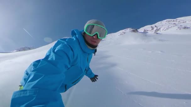 スローモーション セルフィー レンズフレア スノーボーダーは山を下りながらボードで新鮮に落下したパウダースノーを噴霧します 絵のように美しい山と男のスノーボードに冬の太陽が輝いている — ストック動画