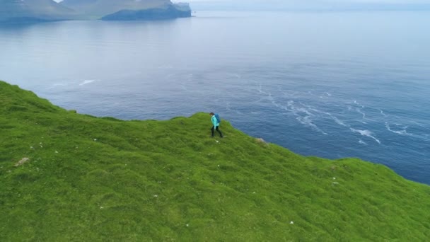 航空写真 美しい海と美しい緑のフェロー諸島の完璧な画像を得るための若い女性カメラマン急な草で覆われた丘をハイキングに沿って飛行 穏やかな山での冒険の女性 — ストック動画