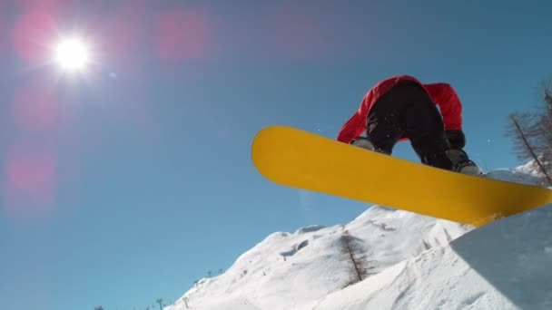 慢动作特写 滑雪者跳大的空气踢腿 喷洒雪花 在完美的冬日飞越太阳 滑雪板在雪地公园里跳跃 阳光从高山上的跳板上照射过去 — 图库视频影像