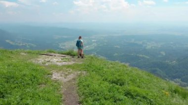 Aktif kadın turistin üzerinden uçarak otlak bir dağın tepesinden manzaralı manzaraya bakıyorlar. Alplerdeki yeşil tepenin zirvesine ulaşan yeşil vadinin güzel görüntüsü.