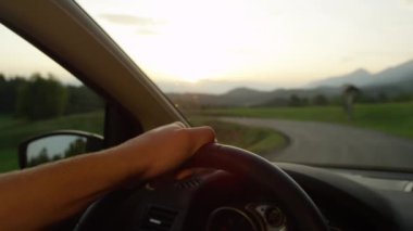 Slow Motion, Close Up, Dof: Gün batımında manzaralı kırsal alanda araba sürerken direksiyonu tutan tanınmayan bir adam. Boş bir yolda, kırsal alanla çevrili sinematik bir yolculuk..