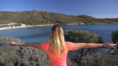 Slow Motion, Close Up: Kendinden geçmiş genç bir kadın vahşi İtalyan adasındaki güneşli turkuaz körfezde ellerini kaldırıyor. Tanınmayan kadın turist deniz kenarına çarpıcı bir bakış açısına ulaşmasını kutluyor.