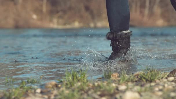 スローモーション ローアングル 認識できない女の子ブーツで浅いストリームに沿って屋外で実行することによって秋を楽しんでいます 暖かい太陽の下で輝く湖の水を撒くのを楽しんでいる精力的な女の子 — ストック動画