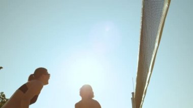 Slow Motion, Low Angle, Close Up, Lens Flare: Neşeli bayan voleybol oyuncuları atlıyor ve sayı yaptıktan sonra beşlik çakıyor. Plaj voleybolu oynarken bikinili, gülümseyen beyaz kadınlar.