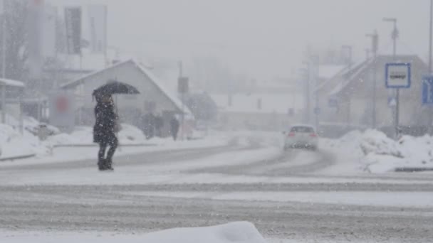スローモーション Dof 認識できない人は 厳しい吹雪の中で滑りやすい雪のアスファルトの道路を渡ります 冬の嵐の間 汚れた通りを歩いている未知の人の映画撮影 — ストック動画