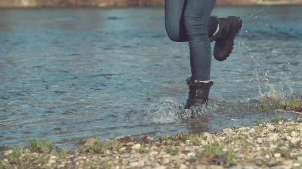 慢动作 低角度 在阳光普照的秋天 穿着毛靴的女人沿着平静的溪流奔跑 一个难以捉摸的爱玩的女孩 一边喝着清澈的湖水 一边享受着秋天 — 图库视频影像