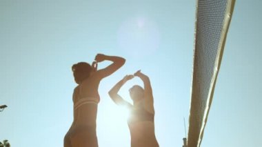 Slow Motion, Low Angle, Close Up, Lens Flare: Mutlu bayan voleybol oyuncuları bir sayı atmayı kutluyor. Tatilde neşeli kadınlar plaj voleybolu oynarken beşlik çakıyor ve yumruk tokuşturuyorlar..
