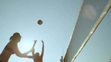 Slow Motion, Low Angle, Close Up, Lens Flare plaj voleybolu oynayan genç bir kadın topu ağların üzerine fırlatıyor. Atletik kızlar güneşli bir yaz gününde voleybol oynarken pas atıyorlar..