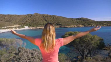 Slow Motion, Close Up: Tanınmayacak kadar neşeli kız İtalyan adasının engebeli kıyılarını izlerken kollarını muzaffer bir şekilde uzatıyor. Yaz tatilindeki mutlu genç bayan turist.