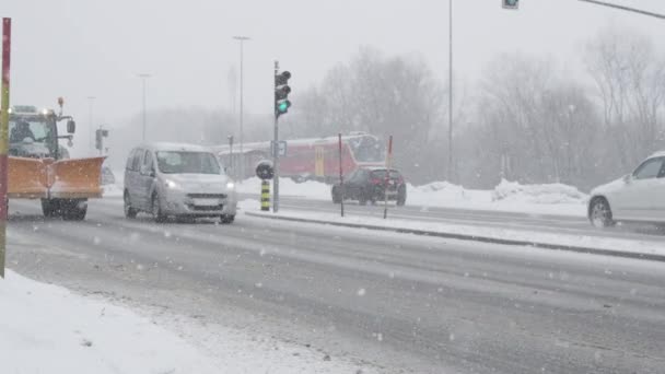 慢动作 在城市的冬季暴风雪中 拖拉机和雪犁以及汽车在雪地的道路上行驶 在极端天气下 车辆驶过绿色红绿灯的电影场景 — 图库视频影像