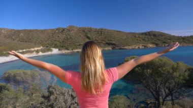 Slow Motion, Close Up: Bilinmeyen kadın turist, uzak bir İtalyan adasının güneşli körfezini izlerken kollarını havaya kaldırıyor. Tanımlanamayan kızın ve Sardunya kıyılarının sinematik çekimi.