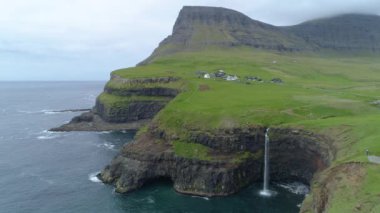 Anteni: Pitoresk Faroe Adaları engebeli kırsal kesiminde çarpıcı şelale güzel manzarasına. Çimenli tepeler ve kayalıklarla uzak köy bulutlu bir günde surround. Engebeli arazi üzerinde bulutlar toplamak.