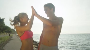 Slow Motion, Lens Flare, Yakından Mutlu Kafkas çiftleri tatilden sonra beşlik çakıyor. Gülümseyen kız arkadaş ve üstsüz erkek arkadaş güneşli bir yaz gününde okyanusun kenarında kutlama yapıyorlar..