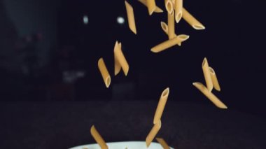 Super Slow Motion Close Dof: pişmemiş makarna havada beyaz plakaya doğru uçuyor. Makarna mermer mutfak tezgahında düşüp tabaktan sekiyor. Uçan makarna sineması