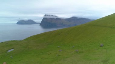 Sersemletici çimen dağları ve uçsuz bucaksız mavi okyanusun yakınındaki boş geniş bir çayırda uçmak. Faroe Adaları 'ndaki sisli bir sabahta engebeli İskandinav manzarasının resimli bir fotoğrafı..