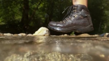 Yarı Sualtı, Yavaş Hareket, Yakın çekim, Kara su geçirmez botlar giyen meçhul kadın yürüyüşçü güneşli bir günde camsı dağ deresine adım atıyor. Kadın ışıldayan nehir suyunu sıçratıyor..