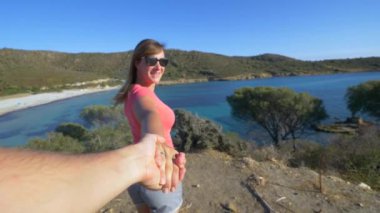 Slow Motion, Pov: Neşeli Kafkasyalı kadın sizi Sardunya 'nın pitoresk sahilinin yukarısındaki görüş açısına götürüyor. Mutlu kız arkadaş güneşli İtalya 'da çarpıcı sahil kenarında yürüyor..