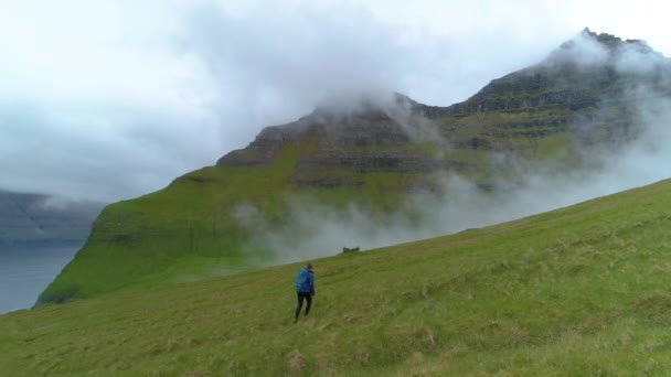 在难以辨认的女人身后飞奔 向深藏在浓云中的长满青草的山 在一个雾蒙蒙的早晨 活跃的女性游客在令人叹为观止的斯堪的纳维亚风景中漫步 — 图库视频影像