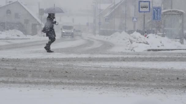 スローモーション Dof 認識できない女性は寒い冬の日に吹雪の中で雪の通りを横断します 激しい吹雪の中を空の雪道を歩いている無名の歩行者 — ストック動画