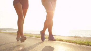Slow Motion, Low Angle, Lens Flare: Deniz kenarındaki manzaralı yolda koşan tanınmayan erkek ve kadın. Güneşli bir günde aktif yaz tatillerinde koşan zinde erkek ve kız arkadaşlar..