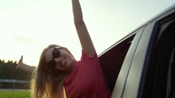スローモーション レンズフレア クローズアップ 幸せな白人の女の子は車の窓を突き出している間に彼女の腕を伸ばします ケアフリーブロンド女性運転にザ牧歌的な田舎で美しい朝 — ストック動画