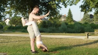 Slow Motion: Bacaklarını üstsüz erkek arkadaşına sarmış genç bir kadın güneşli parkta mekik çekiyor. Neşeli bir çift birlikte beşlik çakarken kız da sallanırken doğruluyor.