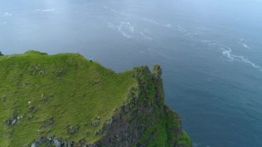 Hava, Zaman Bükülmesi: Genç bayan gezgin muhteşem yüksek çimenli bir uçurumdan fotoğraf çekiyor. Fevkalade mavi okyanus ve beyaz martılar Faroe resimli adalarındaki kayalık siyah uçurumun etrafını sarar..