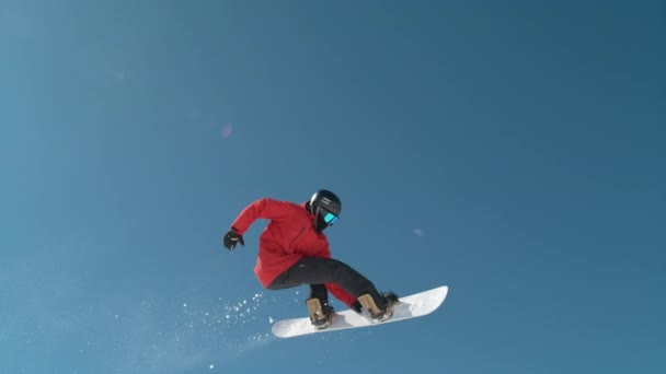 スローモーション閉じる 晴れた山の荒野の澄んだ青い空を飛び越える極端なスノーボーダー 無料のボーダースノーボードやマウンテンスキーリゾートでカメラを飛んでいます スノーボードジャンプ — ストック動画