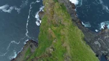 Aerial, Top Down, Copy Space: Resimli Faroe Adaları 'nda tanınmayan kadın turist, çimenli bir uçurumun kenarından fotoğraf çekiyor. Derin bir uçurumun ve derin mavi okyanusun üzerinde uçuyor..