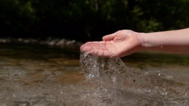 Slow Motion, Close Up, Copy Space: Genç kadın soğuk cam suyu tekrar dağ deresine döküyor. Parlak güneş ışıkları kızın elinde parlıyor Bir avuç ferahlatıcı nehir suyunu topluyor.