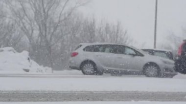 Ağır bir kar fırtınası sırasında arabalar kaygan bir yolda yavaşça yukarı ve aşağı gider. Karlı yolun kenarına park edilmiş siyah bir arabanın yanından geçen trafiğin sinematik görüntüsü. Idyllic kışı.