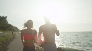 Slow Motion, Close Up, Lens Flare: Güneşli bir yaz gününde sahildeki yaya yolunda eğlenceli bir koşudan sonra gülümseyen erkek ve kadın antrenman partnerleri beşlik çakıyor. Üstsüz adam ve kadın kutlama yapıyor..