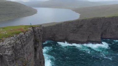 Hava: Genç kadın gezgin için nefes kesici yeşil peyzaj moody Faroe Adaları'nda görmek için bir uçurumun kenarında zamları. İskandinavya hiking kadın hala göl ve dalgalar kayalara çökmesini gözlemler