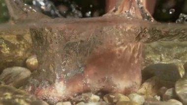 Yarı Sualtı, Yavaş Hareket, Yakın Çekim, Bilinmeyen genç kadın güneşli dağlarda yürüyerek soğuk bir dereye giriyor. Tanınmayan bir kız yalın ayak yürüyüp kristal berrak suyu sıçratıyor..