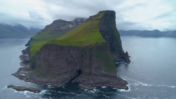 航空写真 美しい風光明媚な山々 と静かな深い青色の海を見下ろす崖の小さな草が茂った島の周りを飛んでください 美しい北欧の田舎の島の素晴らしいショット — ストック動画