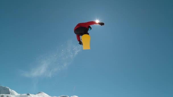 慢动作特写 在阳光灿烂的高山荒野中 极限运动的滑雪者跳过蔚蓝的天空 在高山滑雪胜地 自由式滑板滑雪板和在相机上飞行 跳雪板 — 图库视频影像
