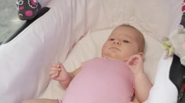 Slow Motion, Close Up, rahat bir arabada uzanan büyük mavi gözlü güzel bir kız çocuğu. Sevimli yeni doğmuş kız ailesiyle parkta yürürken bebek arabasının etrafına bakıyor. Tatlı çocuk yalan söylüyor.