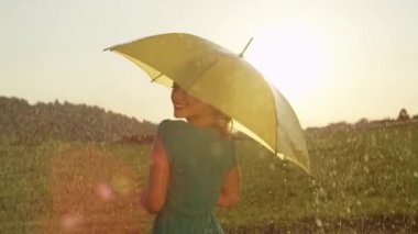 Slow Motion, Close Up, Lens Flare: Gülümseyen sarışın kadın omzunun üzerinden eğlenceli görünüyor ve yaz aylarında serinletici bir yağmurlu günde sarı şemsiyesi ile dönüyor. Bahar yağmurunda dans eden mutlu kız.