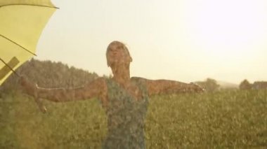 Slow Motion, Close Up, Lens Flare: Yağmurlu bir yaz gününde pitoresk altın ışıklı kırsal sarı saçlı kadın dansları. Kaygısız Kafkas kız onu adil cilt üzerinde ferahlatıcı yağmur damla hissediyor.