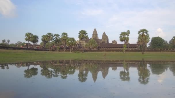 観光客の群衆は息をのむようなアンコールワット寺院の複合体を見るために旅行します カンボジアの崩壊した古代仏教寺院の前の濁った湖とヤシの木の壮大な眺め — ストック動画