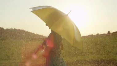 Slow Motion, Close Up, Lens Flare: Serin yaz yağmurunda sarışın at kuyruğu dansları ile muhteşem kadın. Sarı bir şemsiye tutan Kafkas kız altın ışıklı kırsal ortamda yağmurda eğlenceli twirls twirls