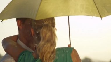 Yavaş Hareket, Yakın Çekim: Genç adam ve kadın küçük sarı bir şemsiye altında bahar yağmuru dönerken birbirlerinin gözlerine bakarlar. Tasasız Kafkas çift dansları yaz yağmurkucakladı.