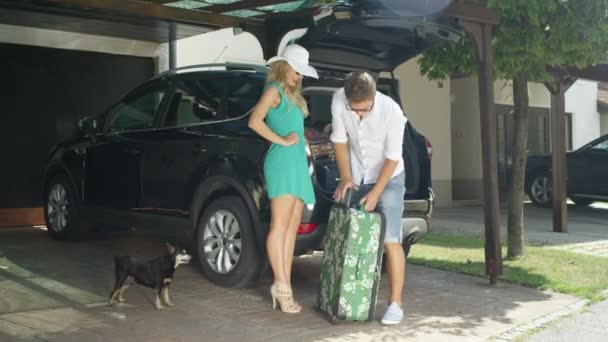 镜头耀斑 快乐的人在和微笑的妻子去度假之前 把沉重的旅行袋塞到了越野车里 新婚夫妇把行李装在停在阳光明媚的车道上的一辆大车的后备箱里 — 图库视频影像
