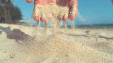 Yavaş Hareket, Yakın Çekim: Tanınmayan genç kadın yumuşak parmak uçları arasında kaba kum eler. Kadın ellerinden uçan ve güneşli egzotik plajüzerine uçan beyaz kum taneleri Sinematik çekim.