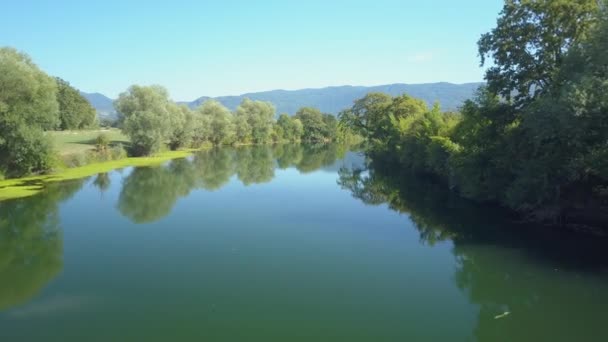 AÉRIAL : Descendre une rivière encore bleu profond traversant un paysage rural ensoleillé de Slovénie. Vue aérienne spectaculaire d'un ruisseau calme traversant les vastes prairies verdoyantes et les terres agricoles de la campagne 