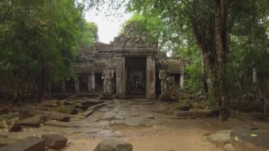 Pov: Çürüyen iki heykel tarafından korunan Budist tapınakkalıntılarına doğru büyük bir taş girişe doğru yürümek. Angkor Wat'ta çürüyen bir dini binanın çarpıcı manzarası, insanlar koridorlarda yürürken